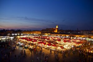 at the heart of Marrakech Jamaa EL Fna. Experience the bustling night market in Marrakesh, Morocco, illuminated against a stunning twilight sky.
