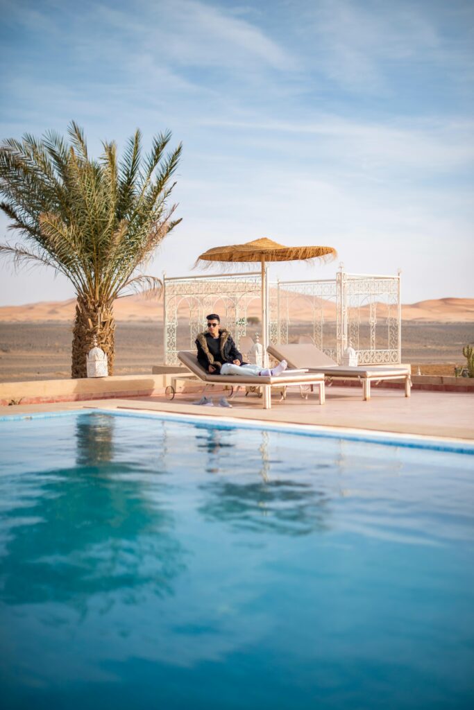 Man lounging by a pool in Merzouga, Morocco with desert views.