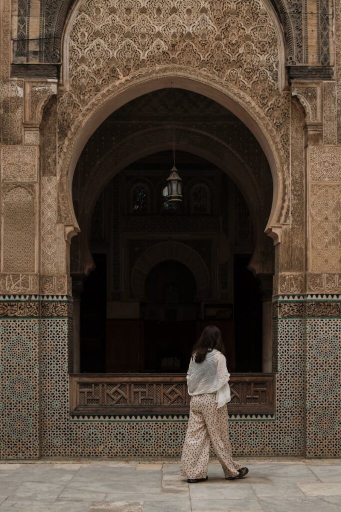 Fes traditional Islamic architecture A woman walks by a beautifully decorated archway of a Moroccan mosque in Fes, showcasing traditional Islamic architecture.