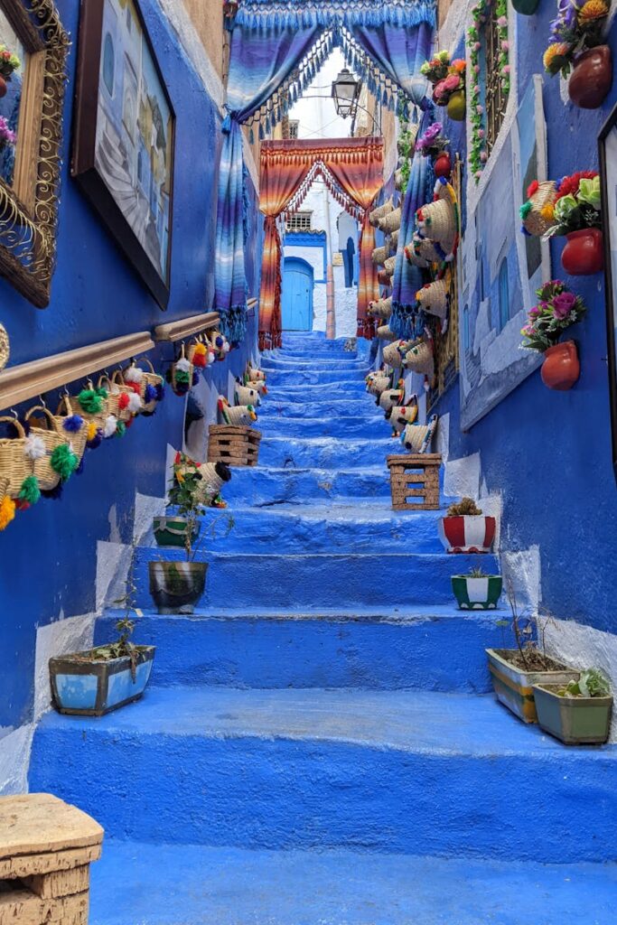 Colorful blue stairway with decorative pots and paintings in Chefchaouen, Morocco.