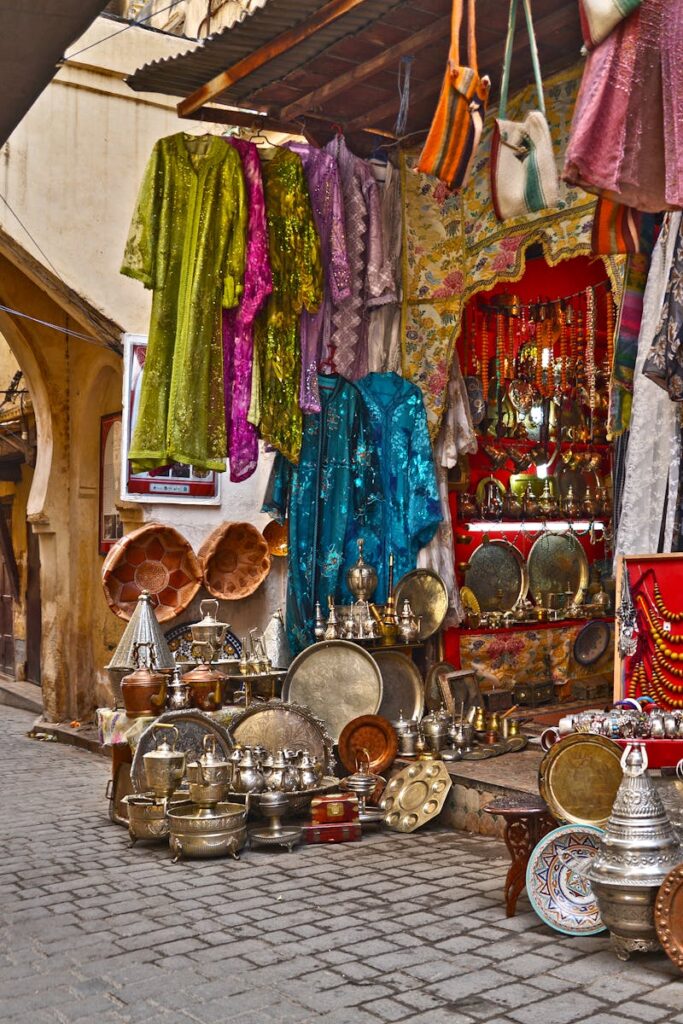 Vibrant market stall in Fès, showcasing colorful fabrics and metalware on display.