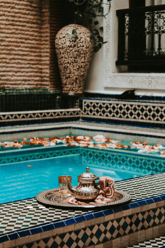 The pleasue of savoring Moroccan mint tea Elegant Moroccan tea setting by a vibrant pool with intricate tile designs in Marrakesh.