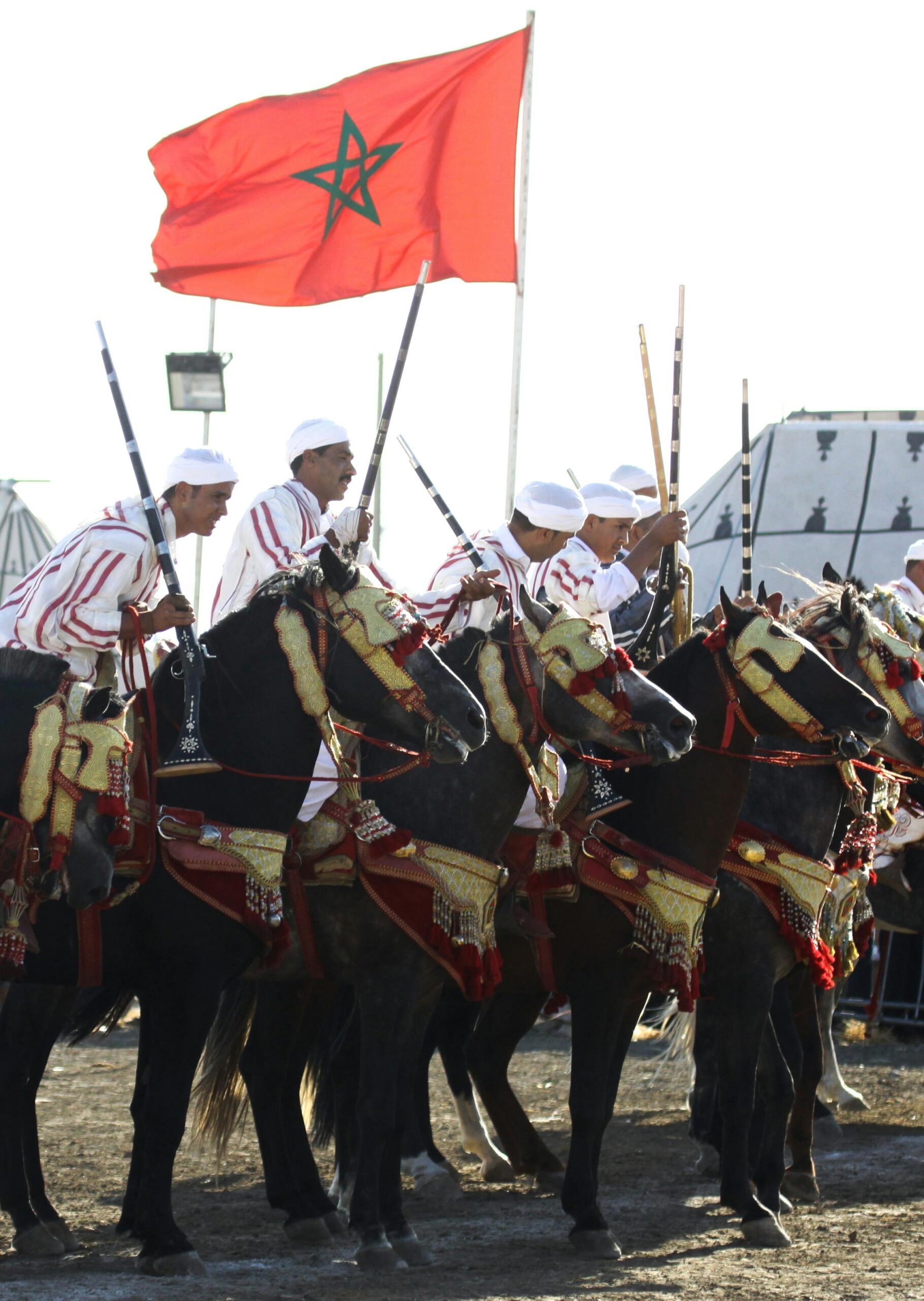 Moroccan riders in traditional Tbourida attire participating in a historic equestrian performance under the Moroccan flag.