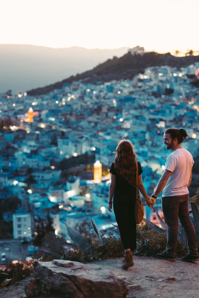 A romantic couple holding hands with a view of Chefchaouen, Morocco at twilight.