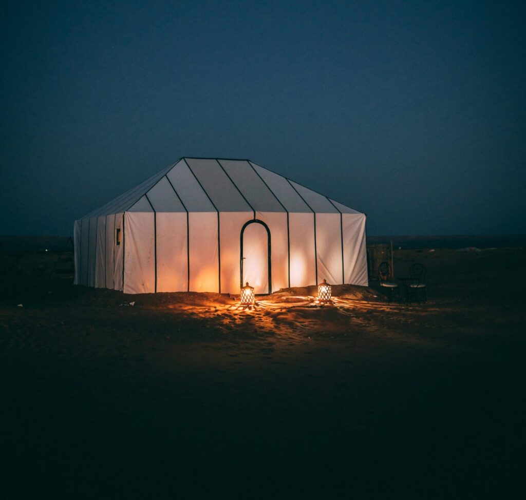 A serene night scene of a glowing tent in the Sahara Desert under a starry sky.