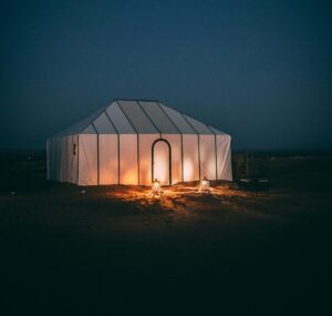 A serene night scene of a glowing tent in the Sahara Desert under a starry sky.