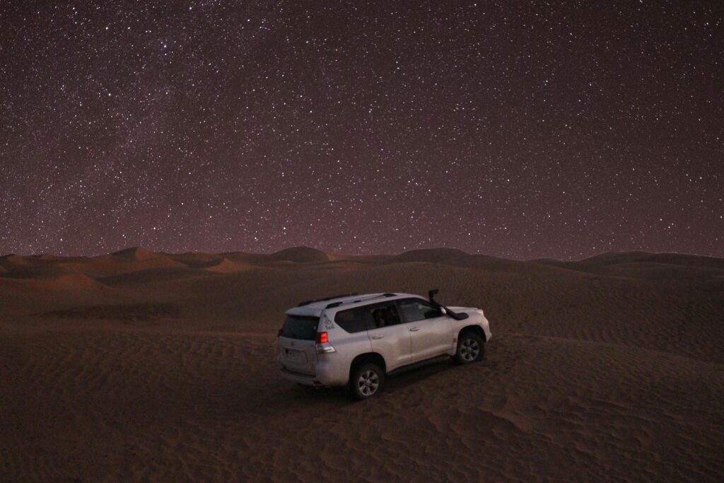 pexels-photo-8369874-8369874-1 A lone car under a starry sky in the picturesque Merzouga sand dunes.